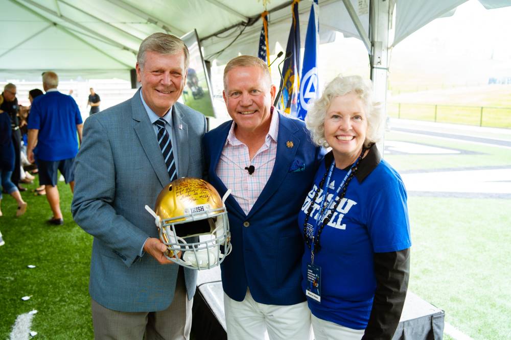 President Tom and Marcia Haas posing together at the Jamie Hosford Football Center dedication. President Haas is holding a golden football helmet.